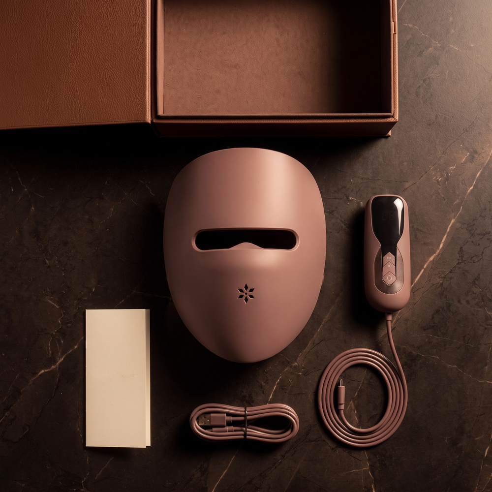 Overhead flat lay of the Luxéra mask, handheld controller, controller cord, charging cable, care guide and presentation case